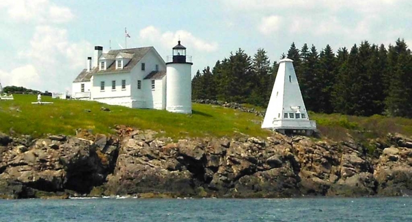 White lighthouse and building rest on a rocky shore. 
